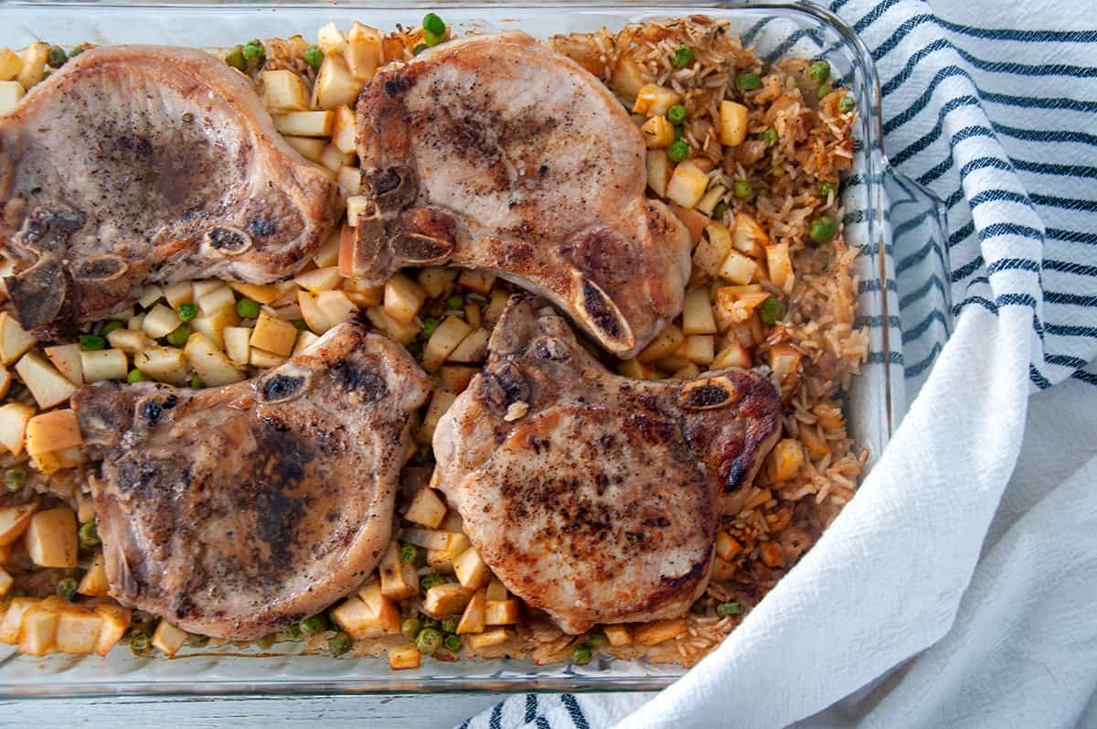 Four baked pork chops on top of a bed of rice and apple medley.