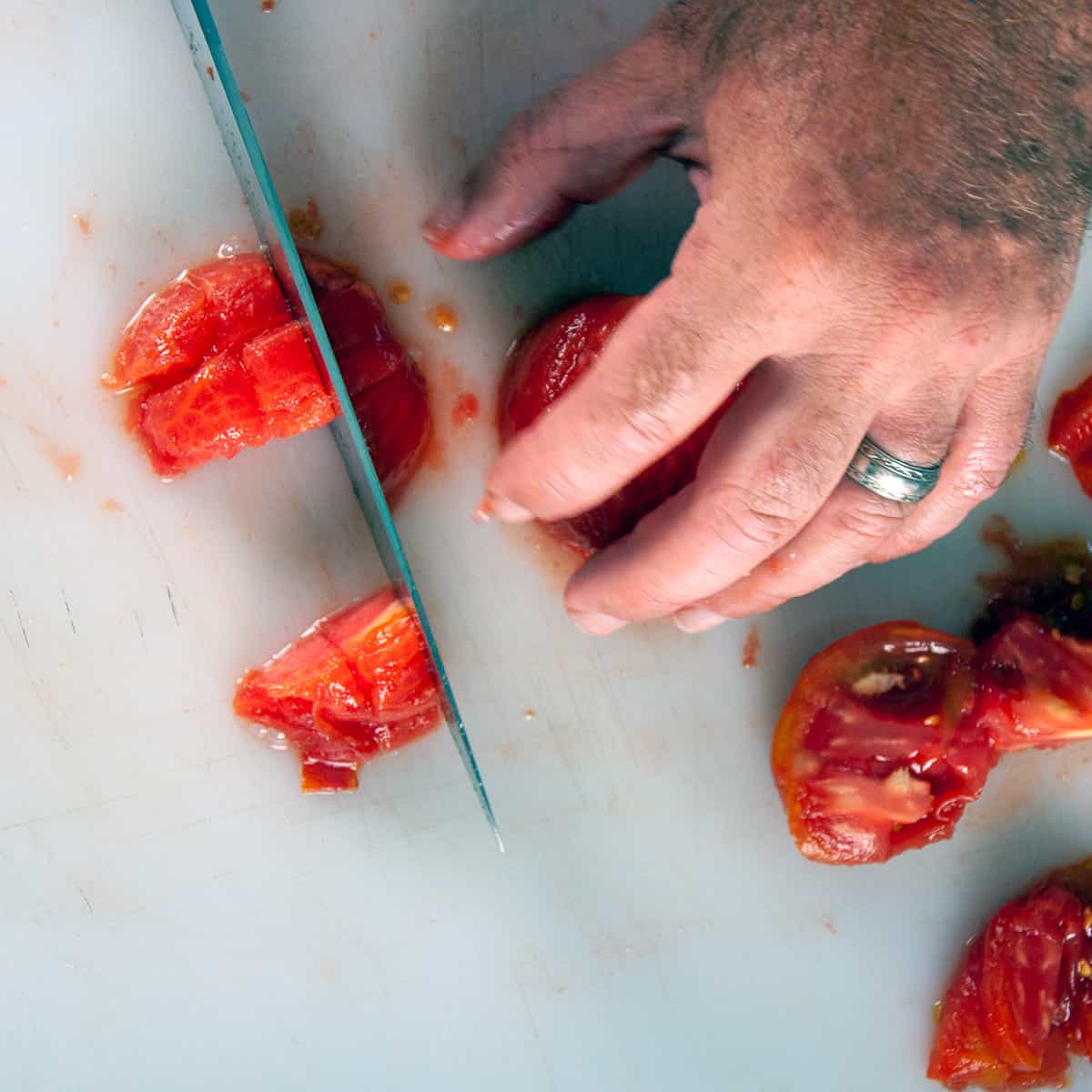 Chopping tomatoes on a white cutting board.