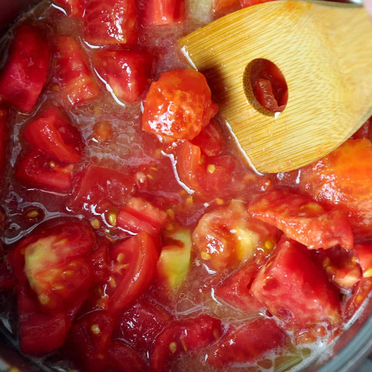 Pot of chopped tomatoes and a wooden spoon in the pot.