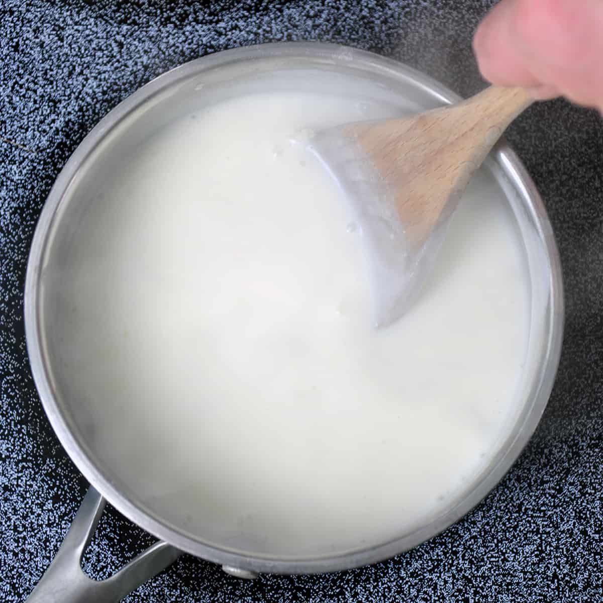 A metal pot with mornay sauce being thickened.