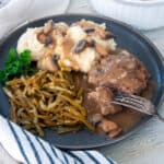 Salisbury steak on a plate with mashed potatoes and green beans.