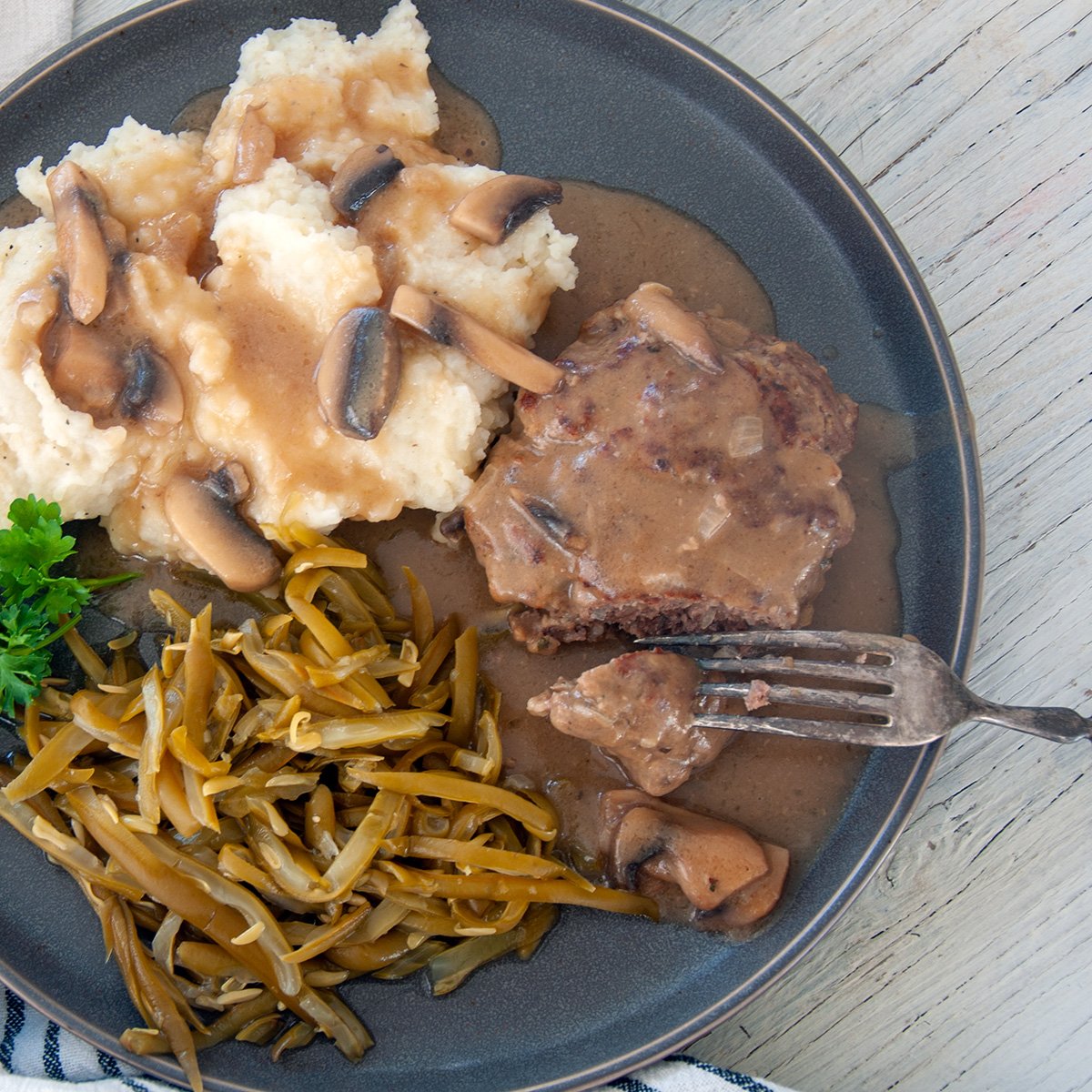 Salisbury Steak on a grey plate with green beans and mashed potatoes.