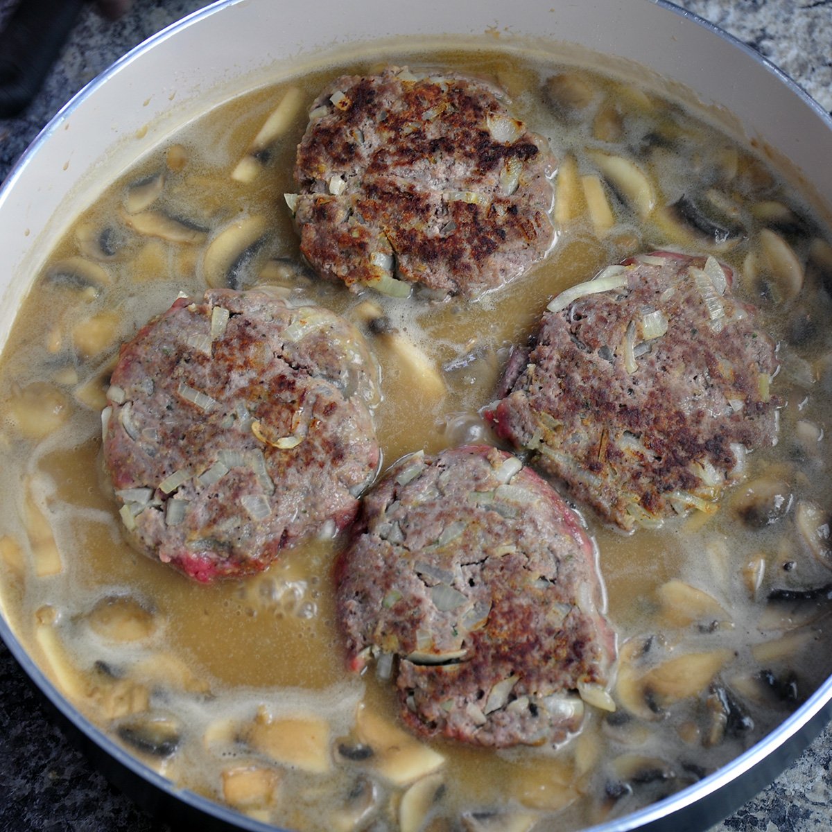 Four steak patties simmering in a saute pan.
