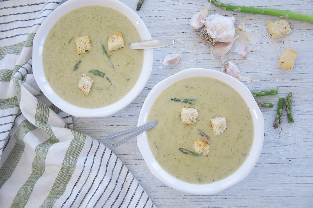 Two bowls of asparagus soup on a white table.