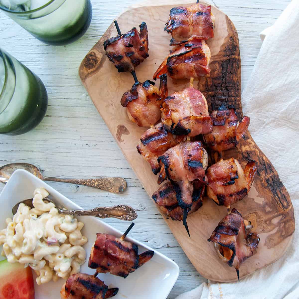 Three skewers of bacon wrapped shrimp on a wood cutting board.