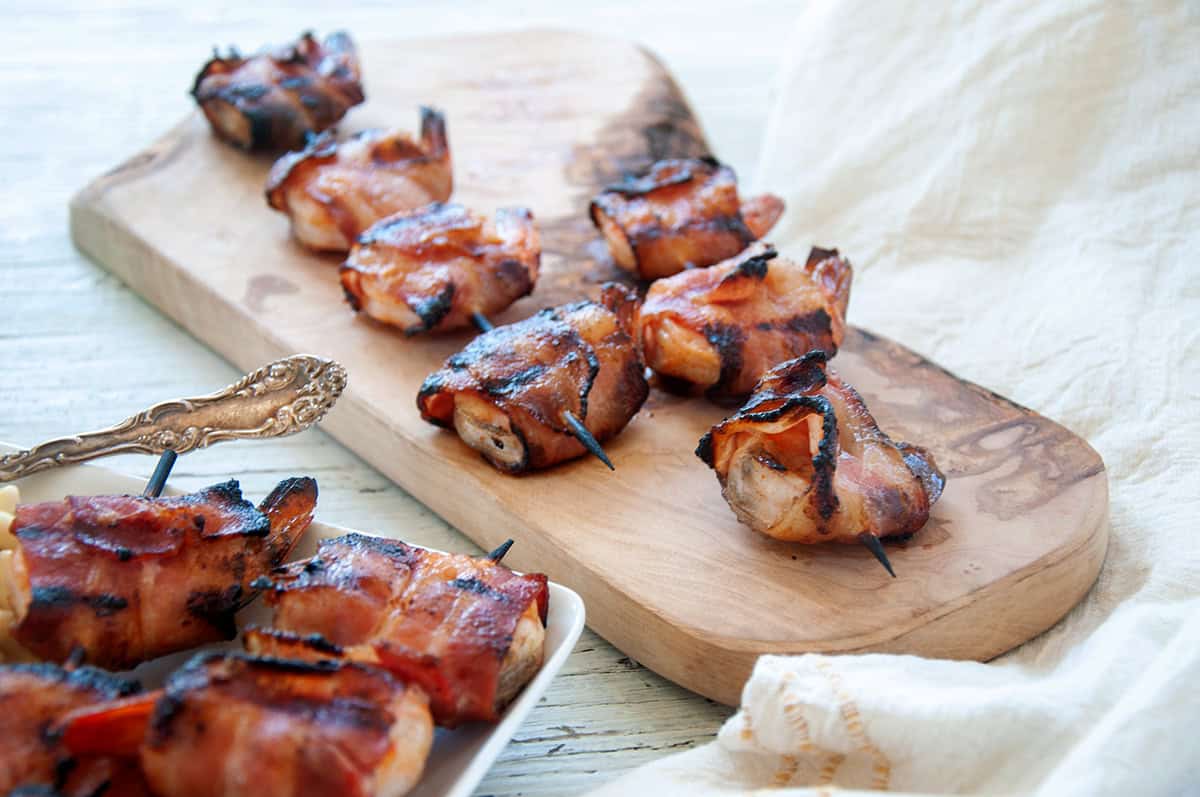 Two skewers of Grilled Bacon Wrapped Shrimp on a wood cutting board.