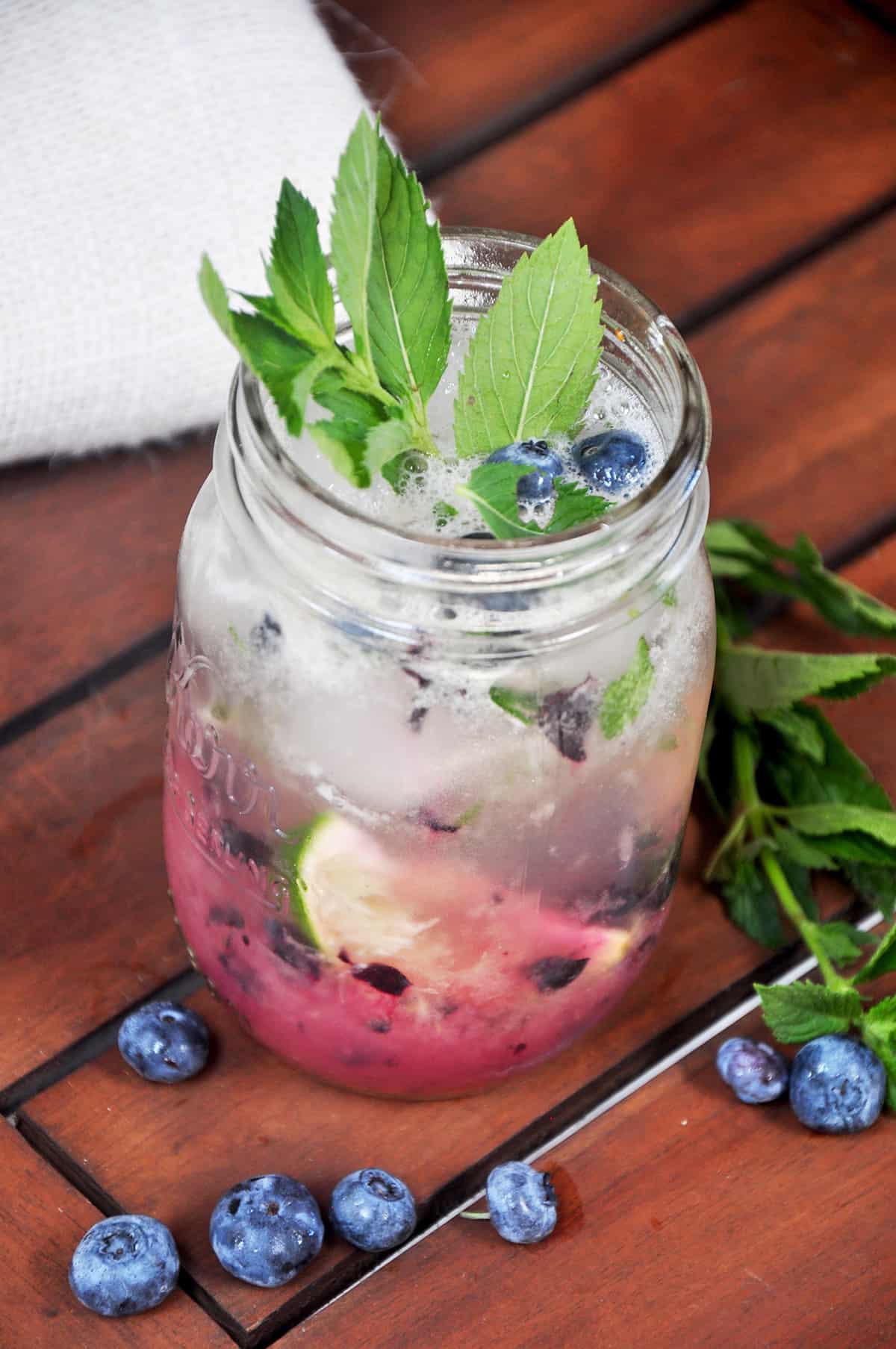 Blueberry Honey Mojito in a small mason jar with fresh blueberries around it.