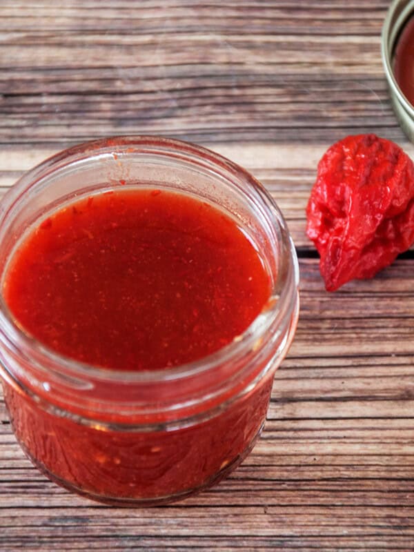 Carolina Reaper Spicy Hot Sauce in a half pint jar. There is a reaper pepper laying next to the jar.