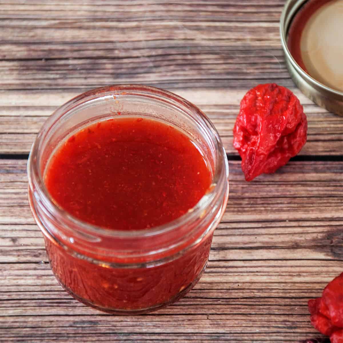 Carolina Reaper Spicy Hot Sauce in a half pint jar. There is a reaper pepper laying next to the jar.