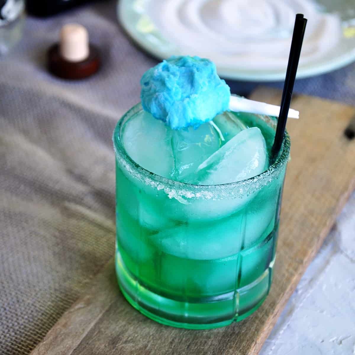 Cotton Candy Margarita on a wood plank with a small cotton candy garnish and two black straws.