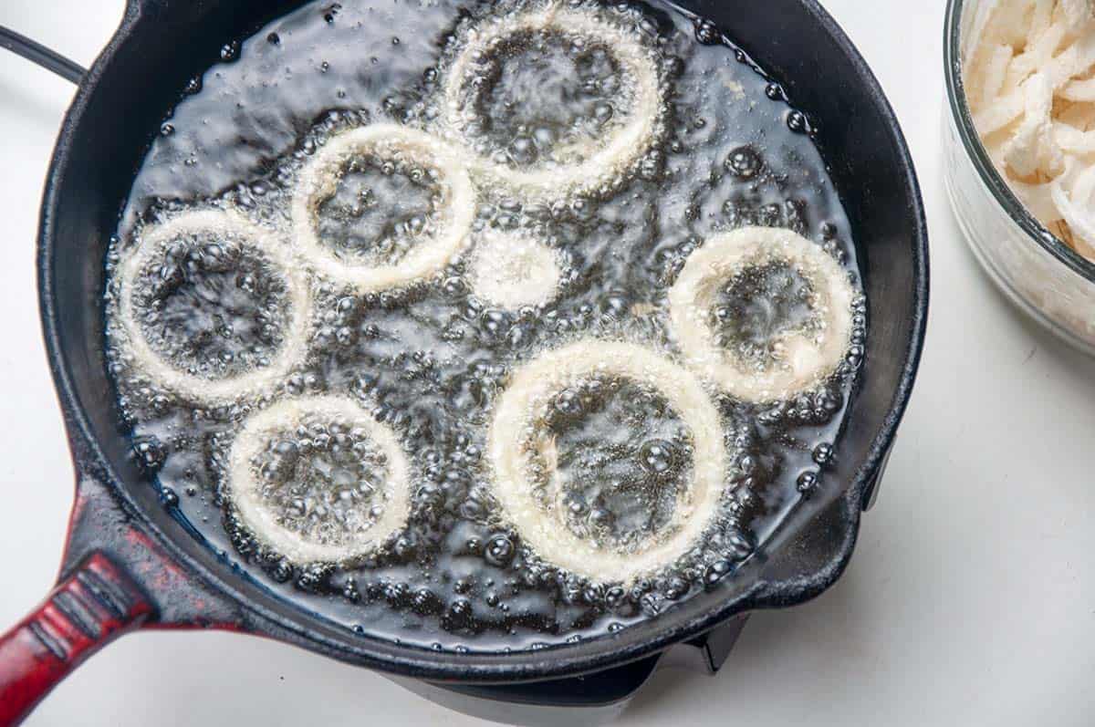 Onion rings frying in cast iron skillet.