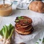 Potato Pancakes on white paper with green onions and applesauce.