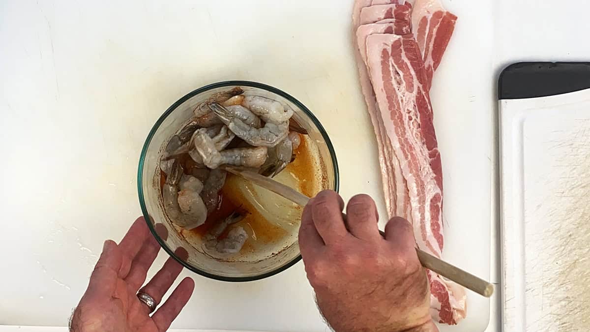 Mixing raw shrimp in a glass bowl with honey lime glaze.