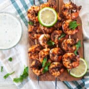 Four blackened shrimp skewers on a wood cutting board with cilantro sprinkled on top.