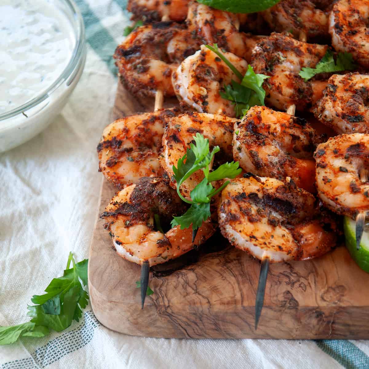 Four shrimp skewers served on a wood cutting board.