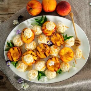 4 Grilled peaches on a big white serving platter topped with the honey whipped mascarpone cheese and mint.