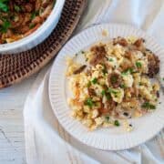 German Käsespätzle dumplings on a white plate with a casserole dish full of it to the side.