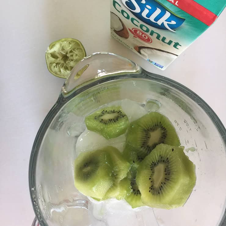 Sliced kiwi in the blender with a carton of Silk Coconut milk displayed in the background.