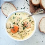 A bowl of Knoephla Soup with parsley sprinkled on top and french bread in the background.