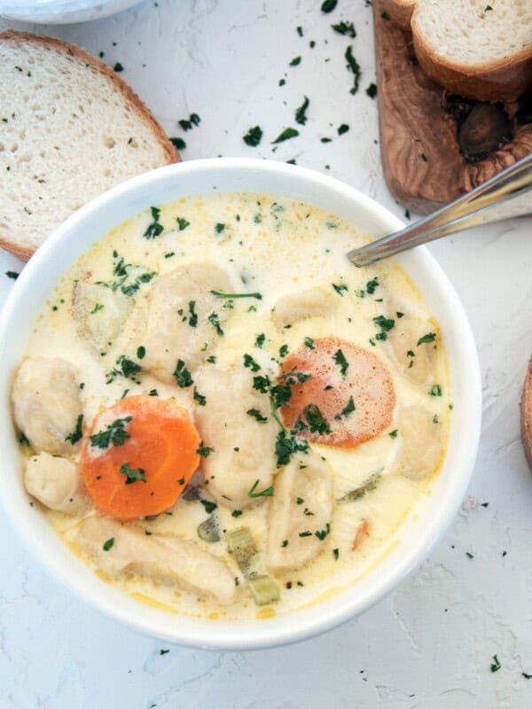 A bowl of Knoephla Soup with parsley sprinkled on top and french bread in the background.