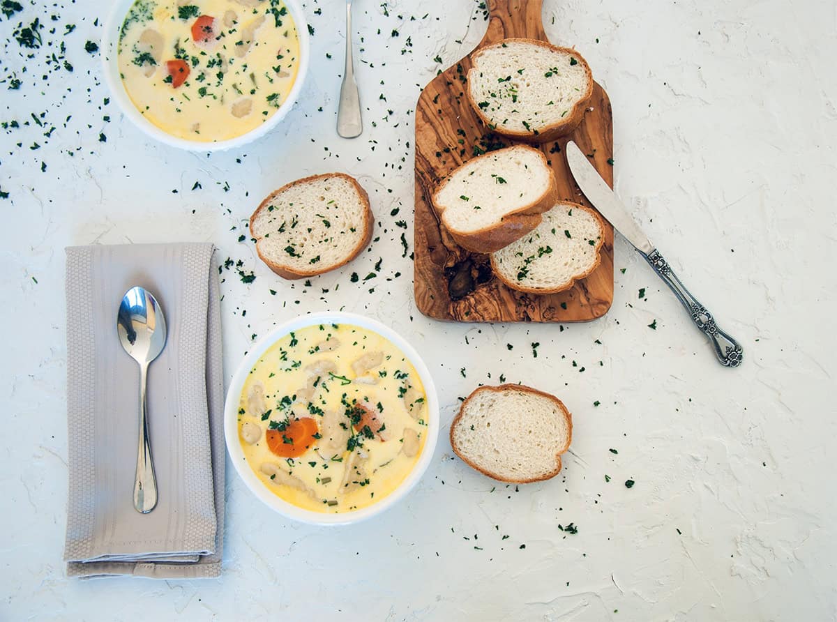 Overhead view of two bowls of knoephla soup. There is a cutting board with some french bread on it.