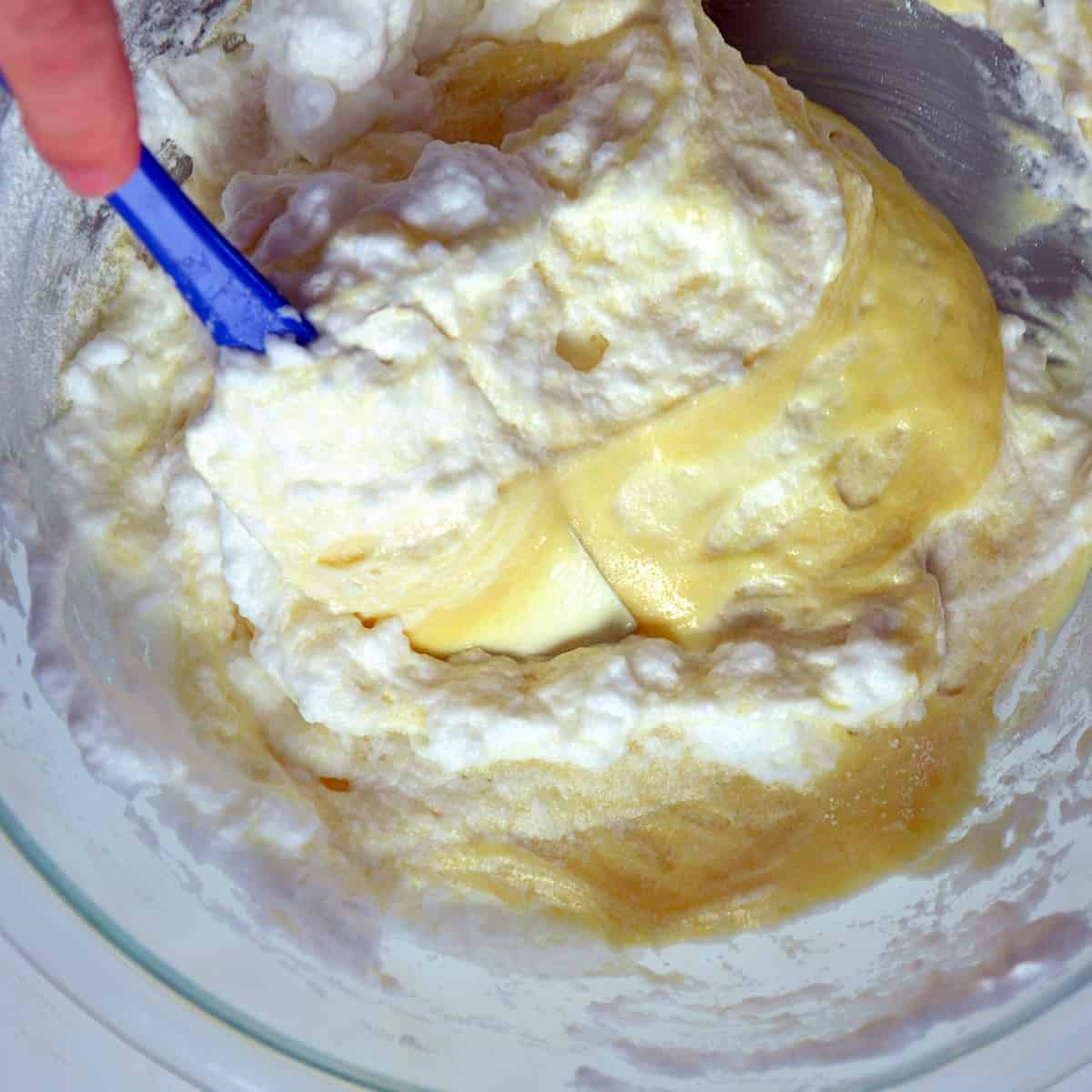 Cake batter and egg whites starting to mix with a rubber spat in the mixture.