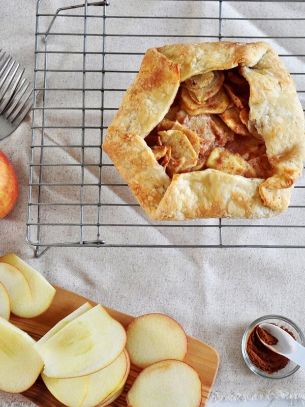 Overhead shot of our apple crostata recipe on a wire tray. There are several cut apples and a small container with cinnamon on it as well.