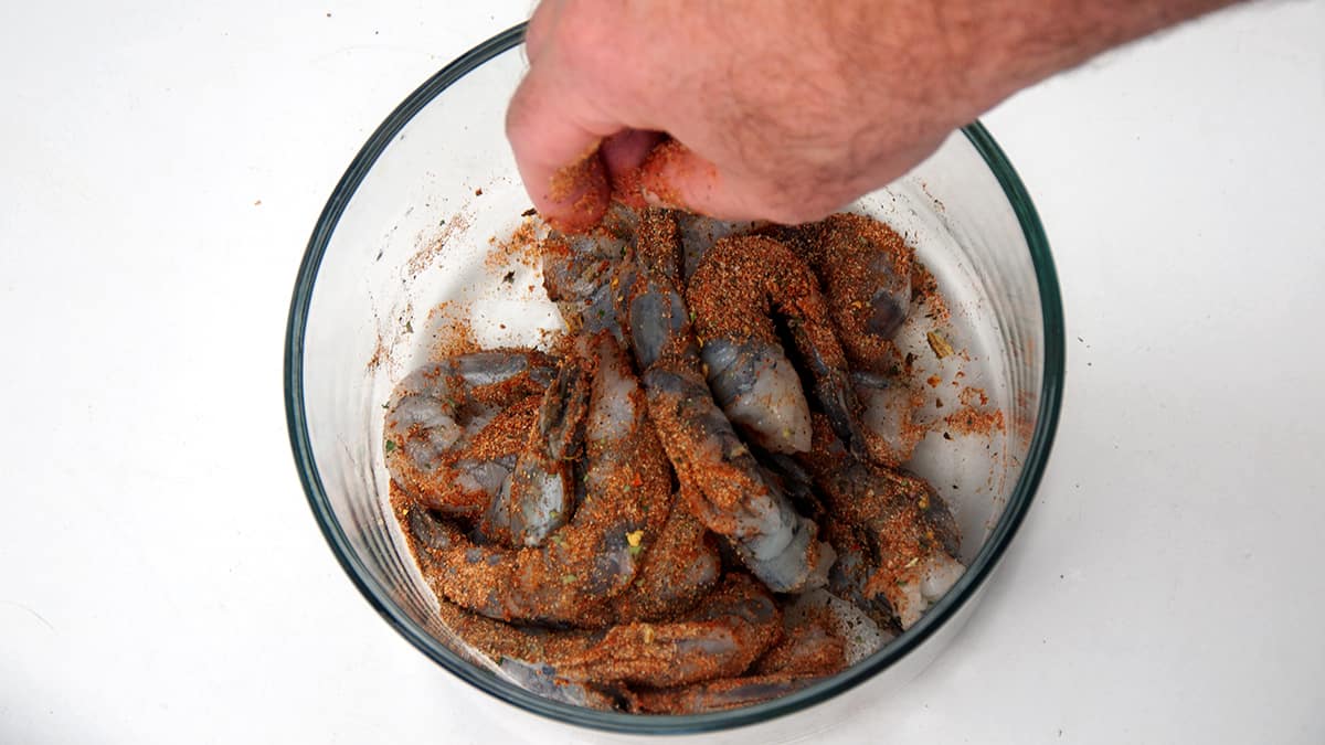 Hand in container spreading blackening spice over shrimp.