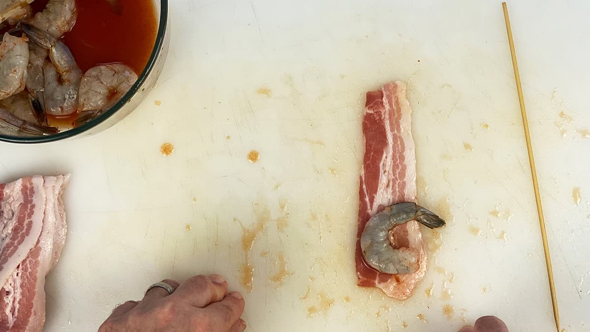 A strip of bacon with shrimp laid out right before it is wrapped.