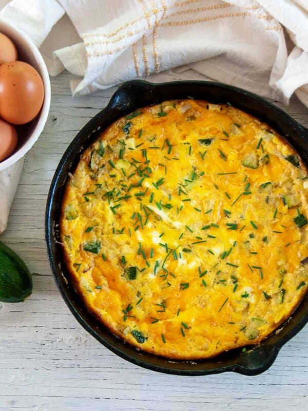 Cast iron skillet with Zucchini Frittata and whole eggs and a raw zucchini to the side.