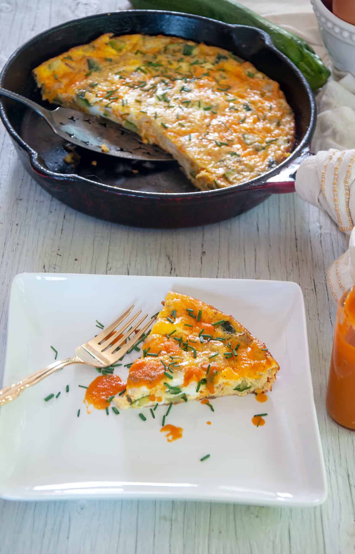 One slice of Zucchini Frittata with hot sauce on top and the rest of the pan in the background.