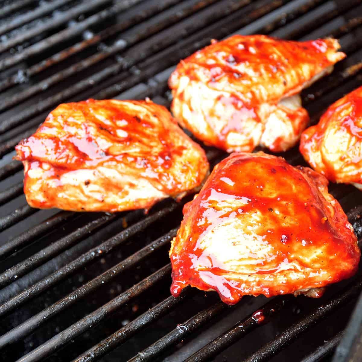 Three barbecue chicken thighs on a grill.
