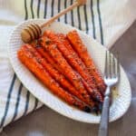 Grilled Carrots on a white plate with a fork and honey spoon.