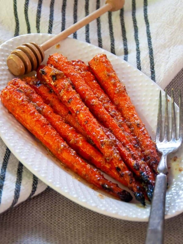 Grilled Carrots on a white plate with a fork and honey spoon.