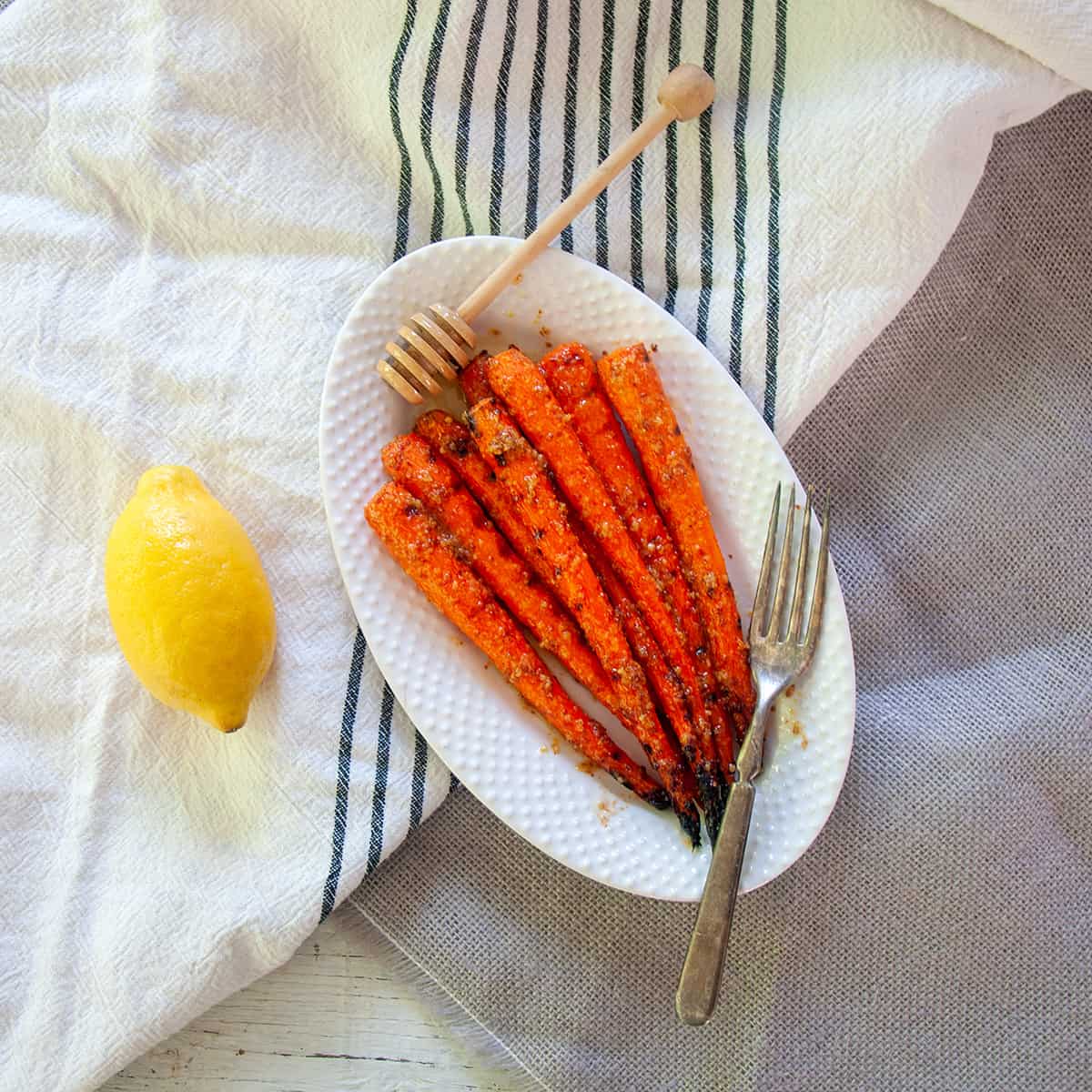 Grilled Carrots on a white plate with a lemon to the side.