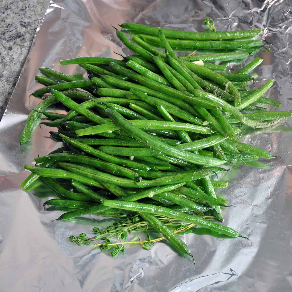 Green beans and fresh thyme sprigs on a piece of tinfoil.