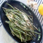 Grilled green beans on a dark plate with parmesan cheese on top.