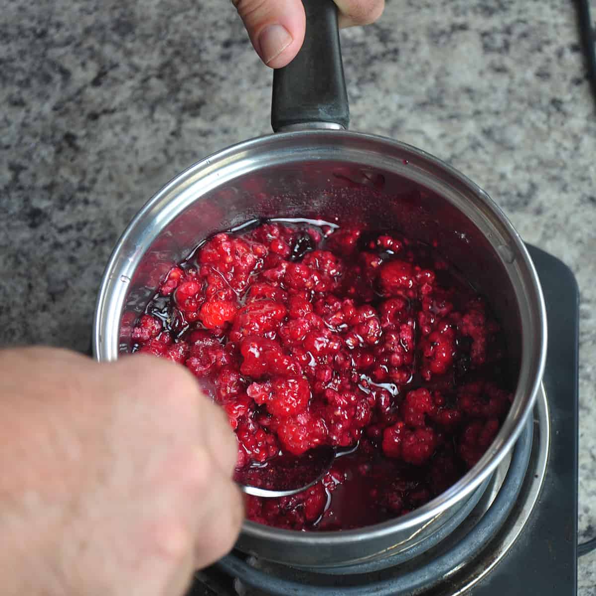 Raspberries,sugar, and black currant jelly in a sauce pan.