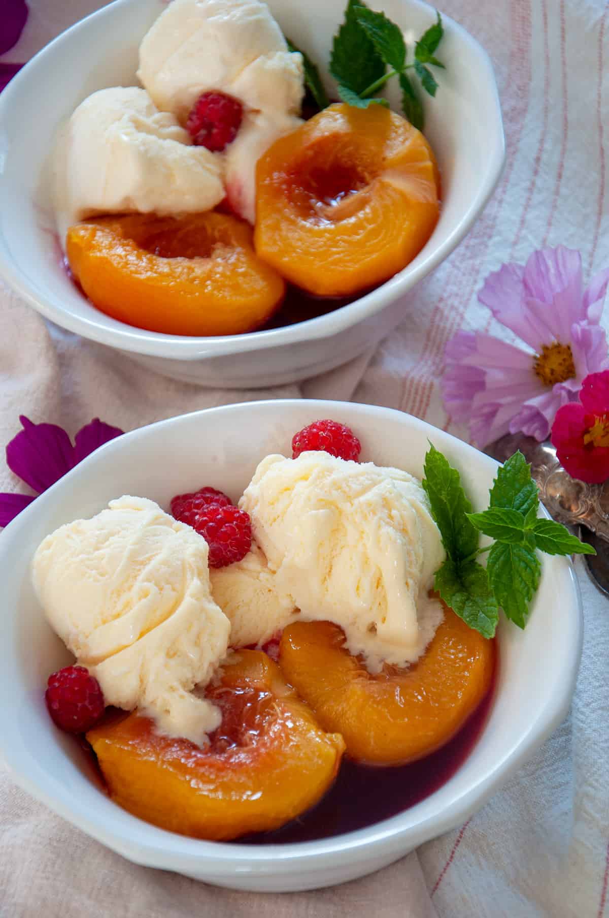 Two bowls of peach melba with some flowers in the background.