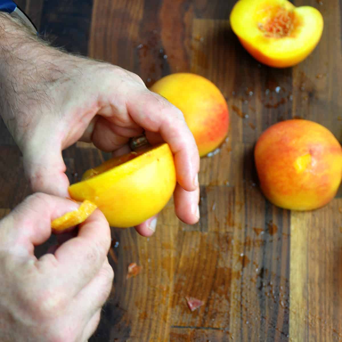 A hand peeling a peach half.