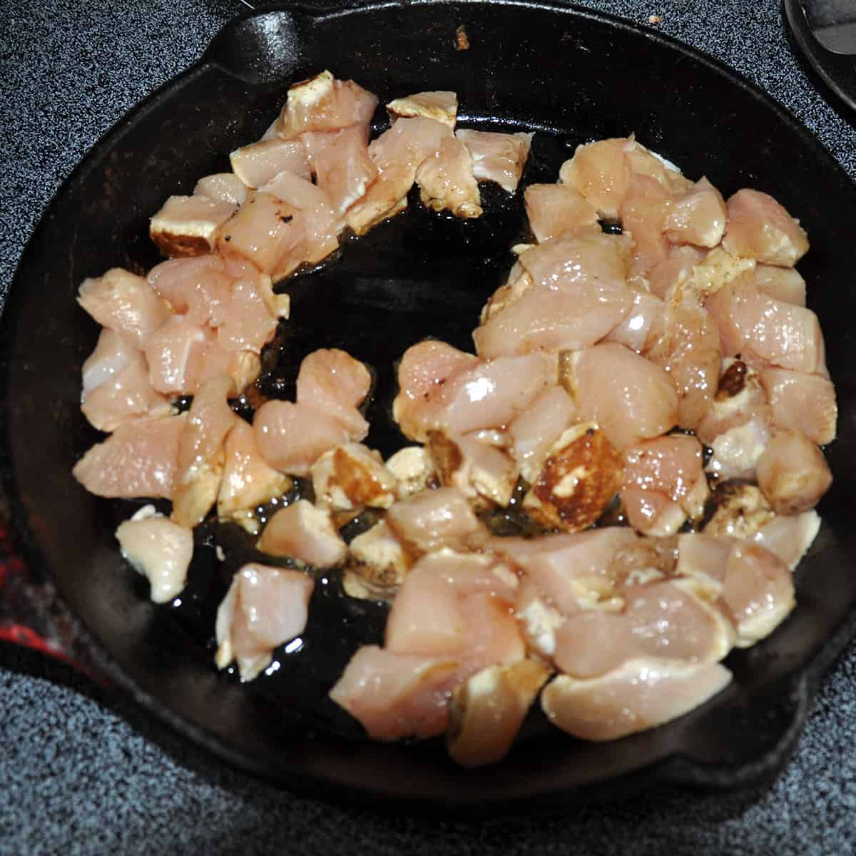 Chicken frying in a cast iron skillet.