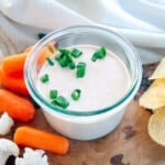 Dip in a bowl with cauliflower, carrots, and chips in the background.