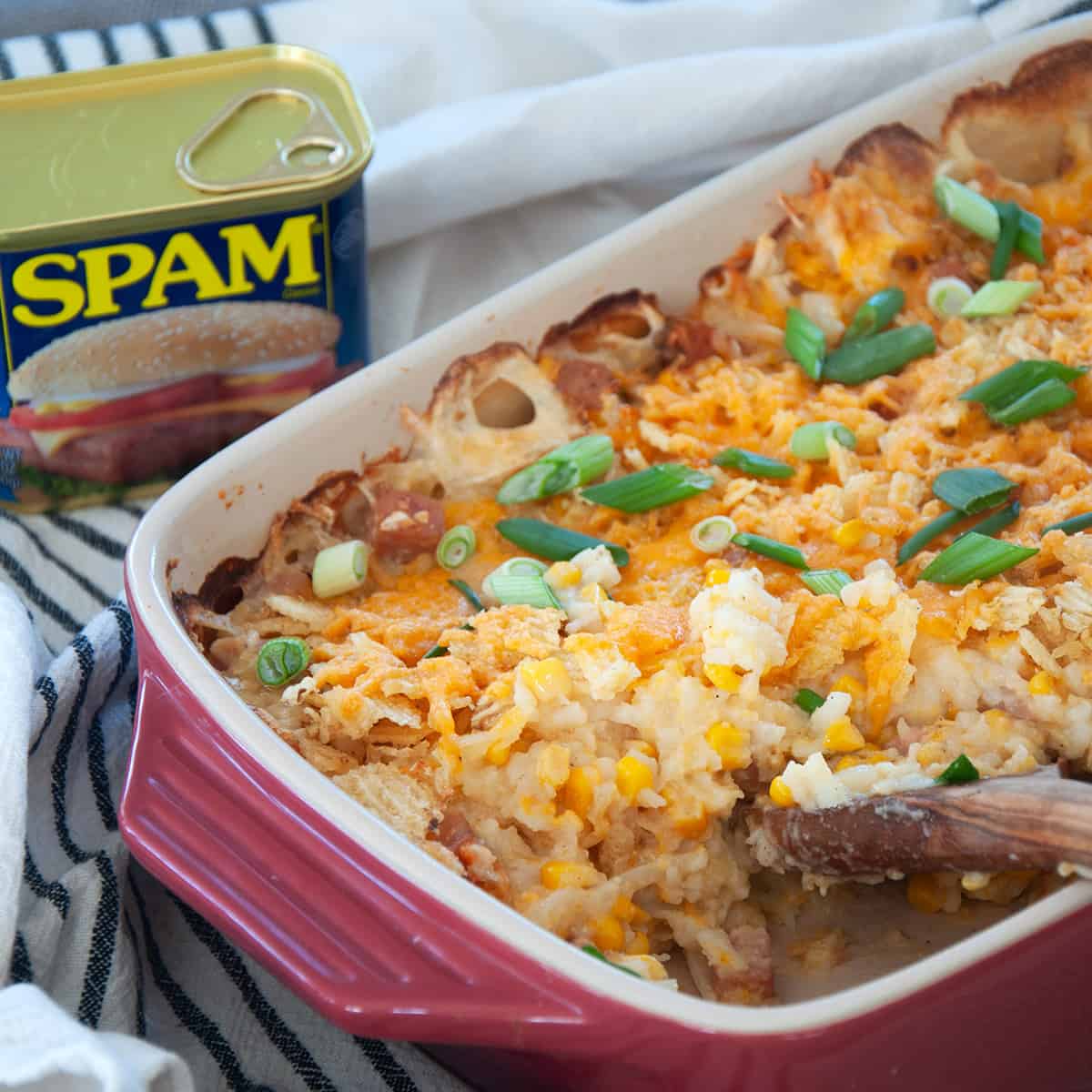 A wooden spoon digging into the casserole dish of finished spam casserole.