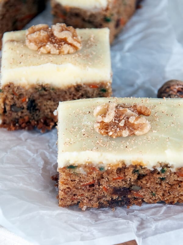 Two pieces of carrot cake bars on a piece of parchment paper.