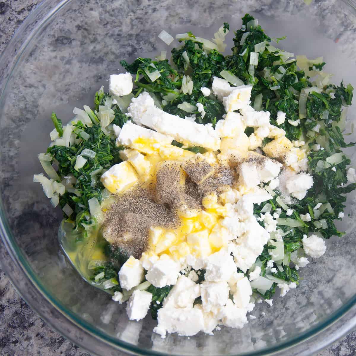 Big glass bowl with feta, eggs, salt, pepper, and spinach mix.