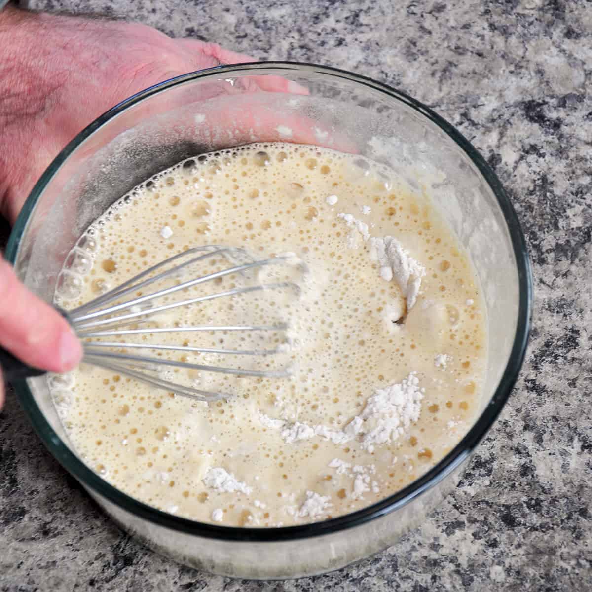 A whisk in a bowl of flour batter.