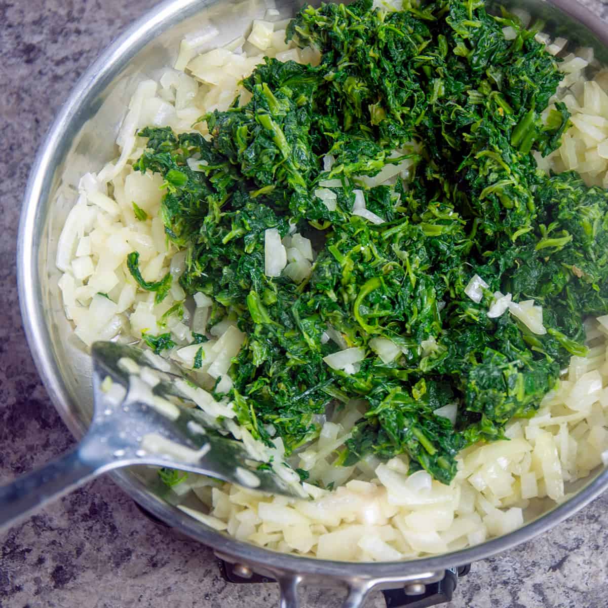 Onions, garlic, and spinach sautéing in a pan.