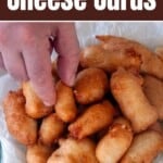 Hand picking up one fried cheese curd in a pile of cheese curds.