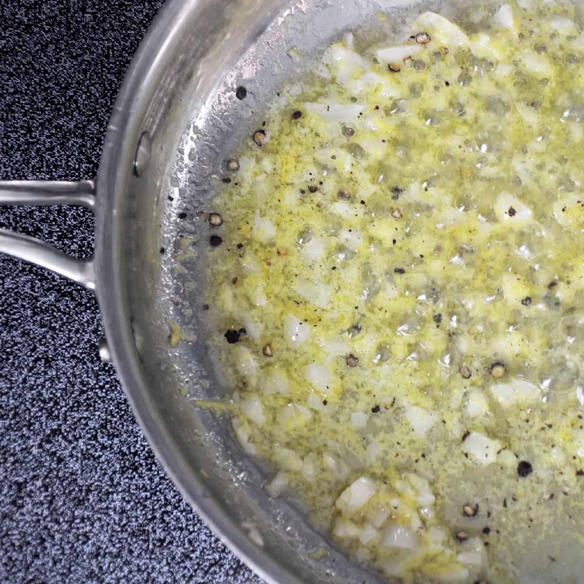 Butter, garlic, lemon zest, and peper simmering in a metal pan.