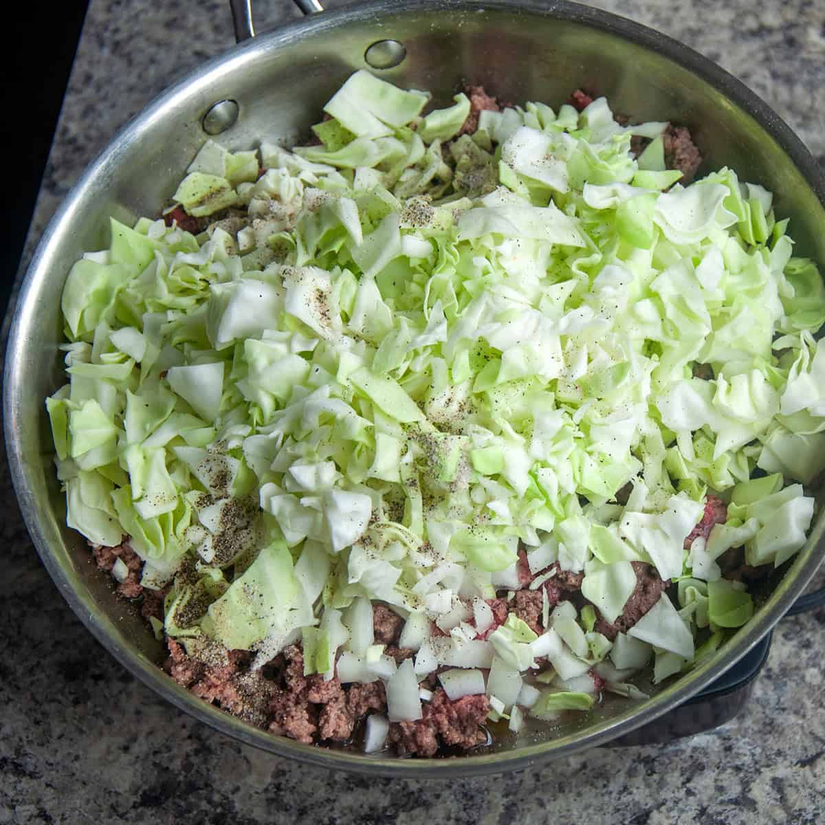 Frying pan with cabbage, burger, onion, garlic, and seasonings showing.